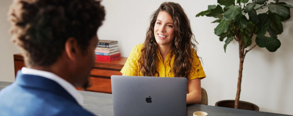 twee mensen in gesprek tegenover elkaar aan de tafel, sollicitatie met Apple laptop