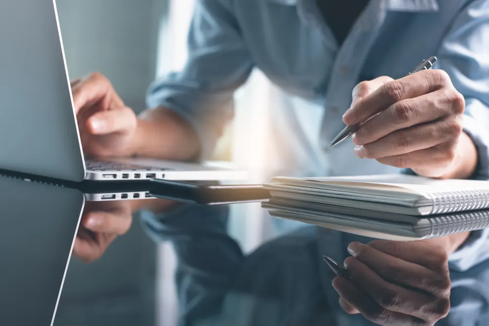 man achter laptop met notitieblok aan het werk, professional