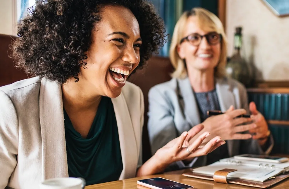 twee vrouwen in gesprek met koffie aan het lachen op werk