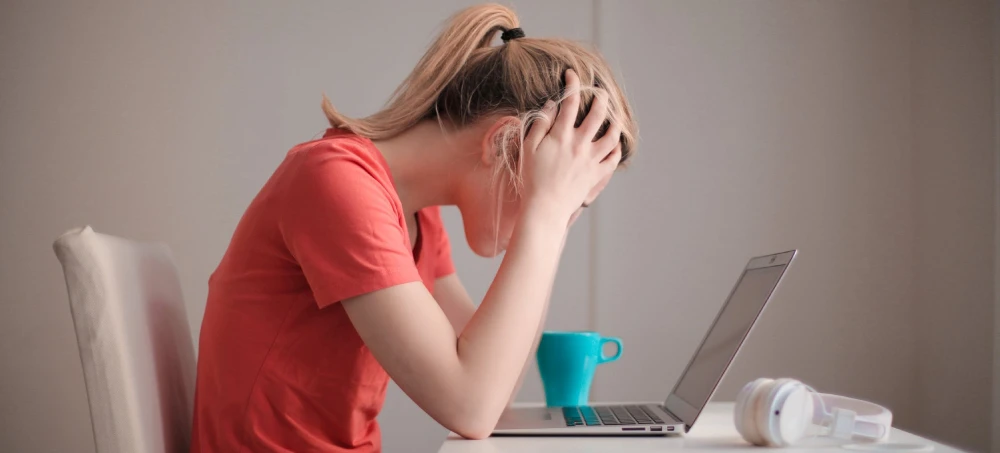 Vrouw met handen in haren achter laptop met koffie heeft faalangst en stress